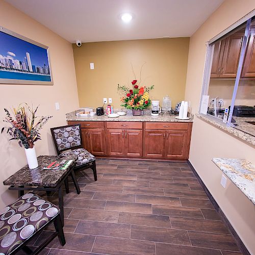 A small waiting area features two chairs, a table with reading materials, a counter with refreshments, floral decor, and a large cityscape picture.