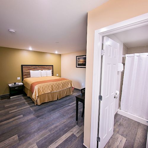 The image shows a cozy hotel room with a bed, nightstands, a window, and an adjacent bathroom with a shower.