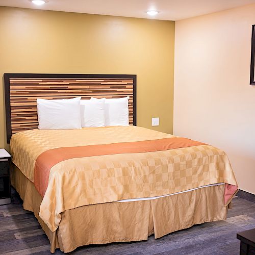 A neatly made bed with a two-tone headboard in a cozy, well-lit room, featuring a nightstand and a framed picture on the wall.