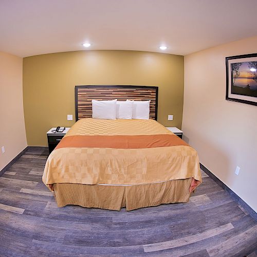 This image shows a neatly arranged hotel room with a double bed, two bedside tables, framed artwork, and wooden flooring, looking cozy and inviting.