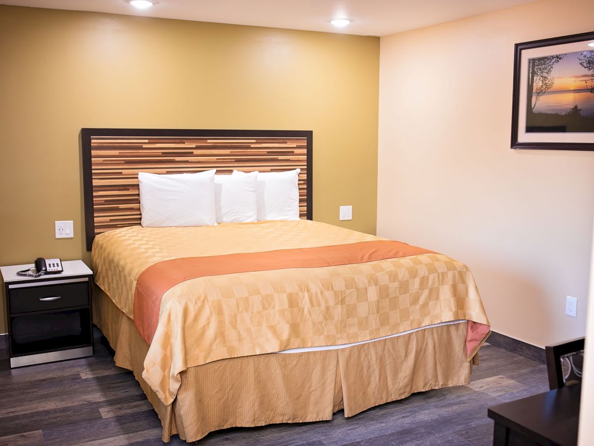 A neatly made bed in a hotel room with a framed picture on the wall and a nightstand with a phone.