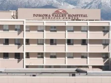 The image shows a multi-story building identified as Pomona Valley Hospital, with snow-capped mountains in the background surrounded by some trees.